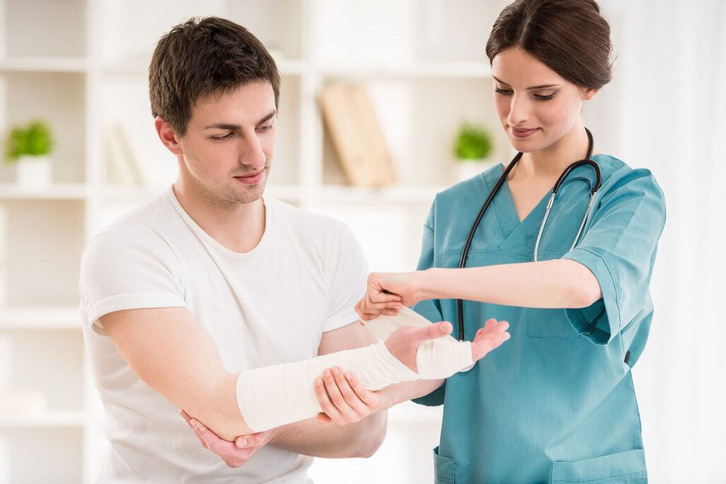 Young nurse with stethoscope bandaging hand of male patient.